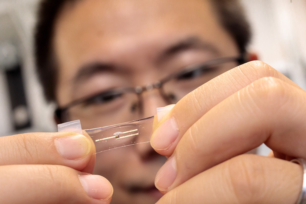 A researcher stretches the clear neuromorphic chip with his thumbs and index fingers.