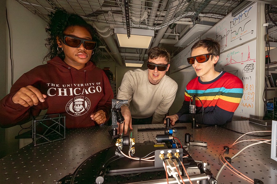 Two students and an instructor examine an optical table